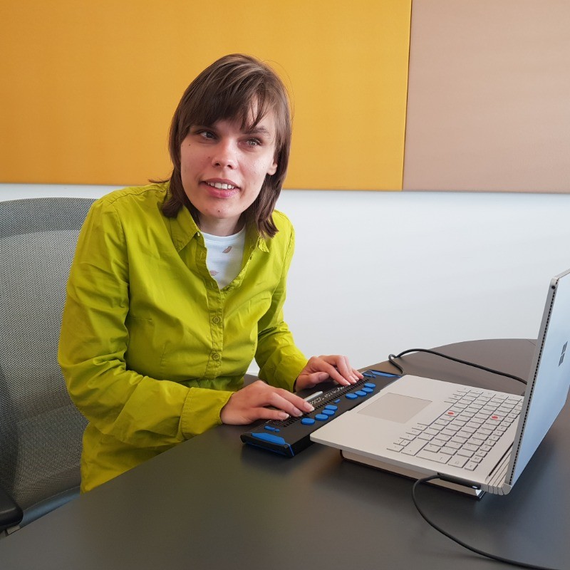 Franziska schaut in die Kamera an einem Laptop mit Braille Zeile